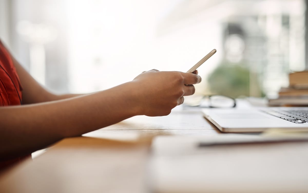 Close-up of a person using a smartphone and laptop to manage their NDIS plan and research registered service providers.