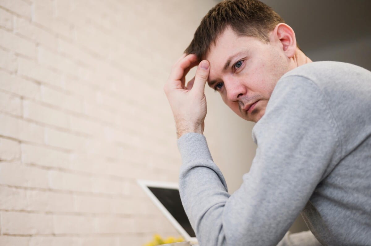 A man resting his head on his hand looking stressed and overwhelmed next to a laptop, representing sensory overload in adults.